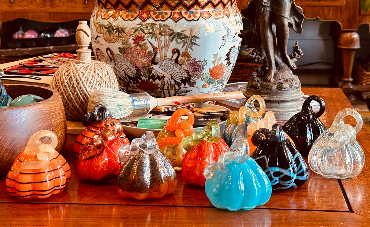 Colorful glass pumpkins on a wooden table with decorative items in the background
